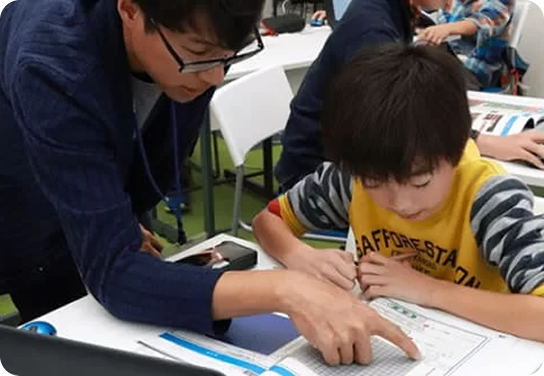 プロクラの授業 講師が男子生徒のノートに指をあてて教えている様子