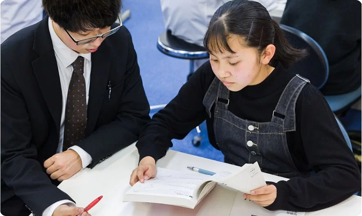 真剣な表情で教科書を開き講師に相談する女子生徒の様子